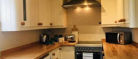 A compact kitchen with white cabinets, a washing machine, a stove, and a microwave.