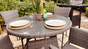 A round outdoor table with two plates, cutlery, and a glass of water, surrounded by wicker chairs. - Vineyard Cottage Sleeps 4 with Garden (Norwich)