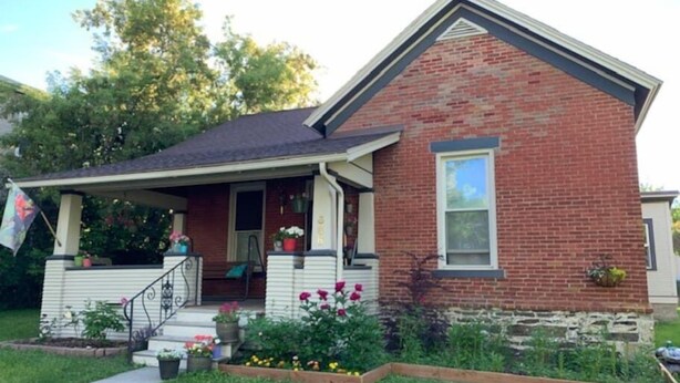A two-story brick house with a front porch, a small garden, and a flag. - Trip6 Historic Brick Home (Helena)