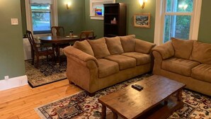 A living room with two sofas, a coffee table, a dining table with chairs, a bookshelf, and a ceiling fan. - Trip6 Historic Brick Home (Helena)