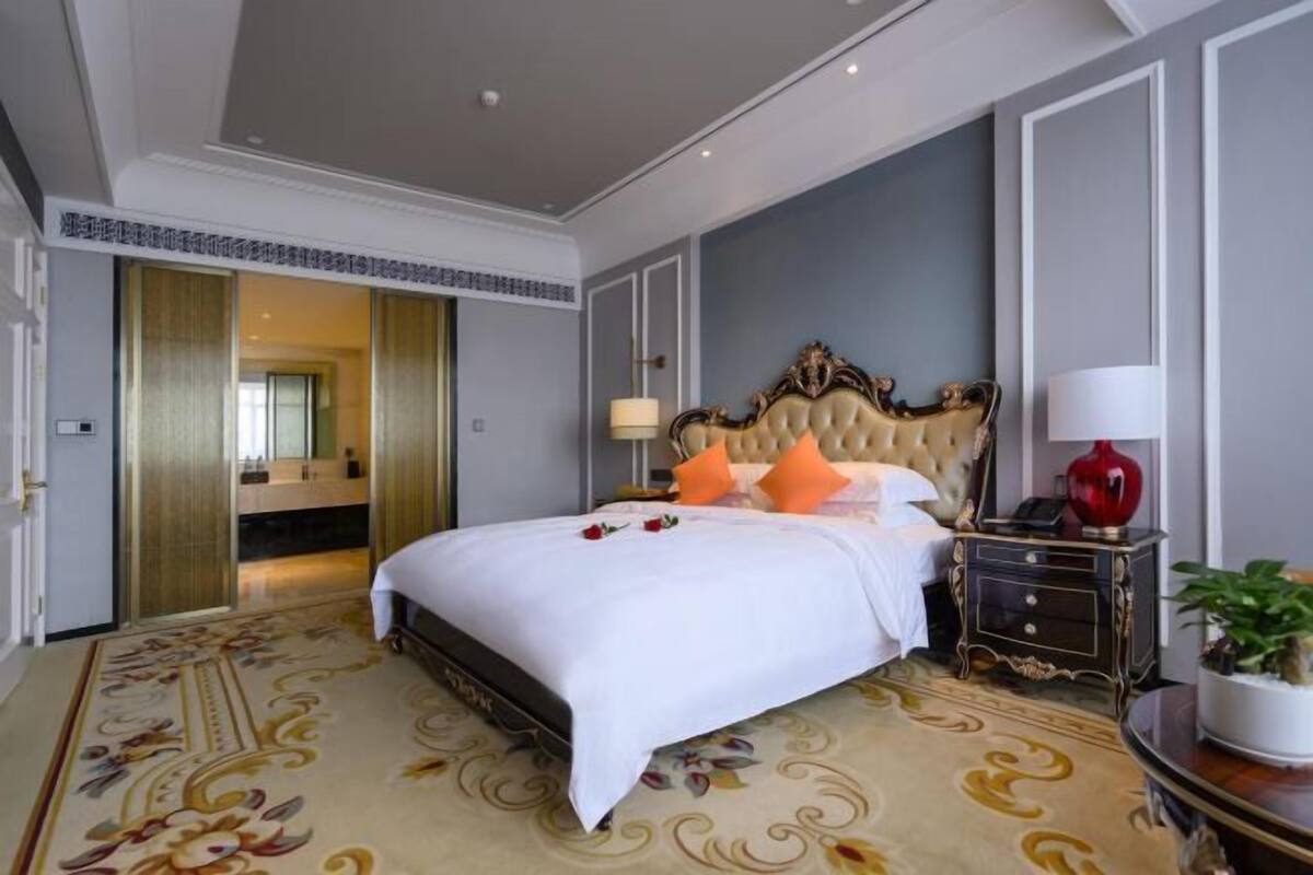 Une chambre spacieuse avec un grand lit, une tête de lit décorée et une moquette à motifs floraux.