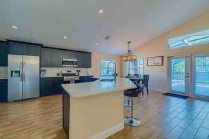 A modern kitchen with dark cabinets, stainless steel appliances, and a central island. - Spacious Getaway ~ Heated LED Pool & Ping Pong (Minneola)