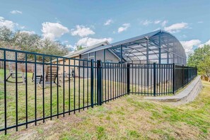 A greenhouse structure with a metal fence surrounding it. - Spacious Getaway ~ Heated LED Pool & Ping Pong (Minneola)
