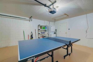 A ping pong table in a room with white brick walls, a door, and a shelf with cleaning supplies. - Spacious Getaway ~ Heated LED Pool & Ping Pong (Minneola)