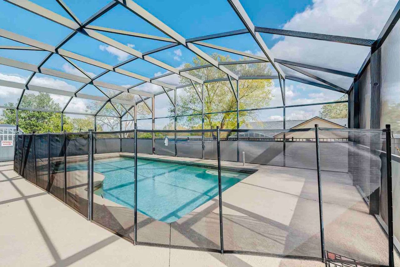 A covered outdoor swimming pool with a glass enclosure, surrounded by a metal fence.