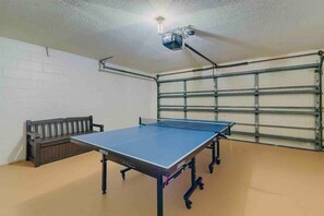 A ping pong table in a room with a white brick wall and a garage door. - Spacious Getaway ~ Heated LED Pool & Ping Pong (Minneola)