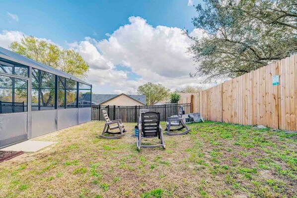 A backyard with a wooden fence, a covered patio area, and three rocking chairs. - Spacious Getaway ~ Heated LED Pool & Ping Pong (Minneola)