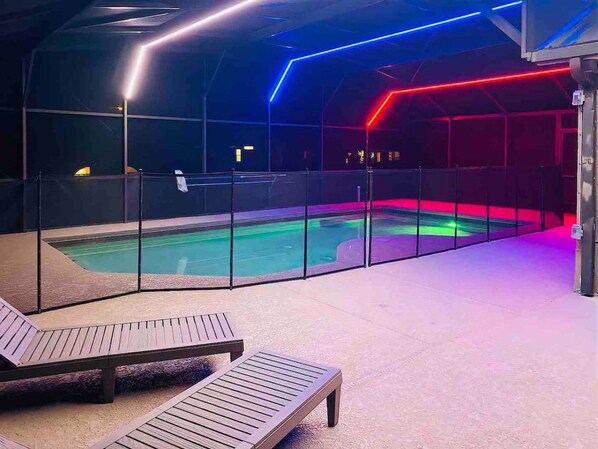 An indoor swimming pool area with lounge chairs and a glass barrier. - Spacious Getaway ~ Heated LED Pool & Ping Pong (Minneola)