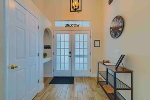 A hallway with a double door entrance, a welcome sign, a wall clock, and a desk with a computer. - Spacious Getaway ~ Heated LED Pool & Ping Pong (Minneola)