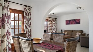 A dining area with wicker chairs, a wooden table, and a large window with curtains. - Villa Serendipity with Mountain View, Private Heated Pool & Wi-Fi (Playa Blanca)