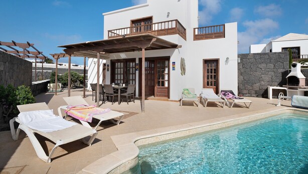 A modern villa with a pool, outdoor seating, and a stone wall. - Villa Serendipity with Mountain View, Private Heated Pool & Wi-Fi (Playa Blanca)