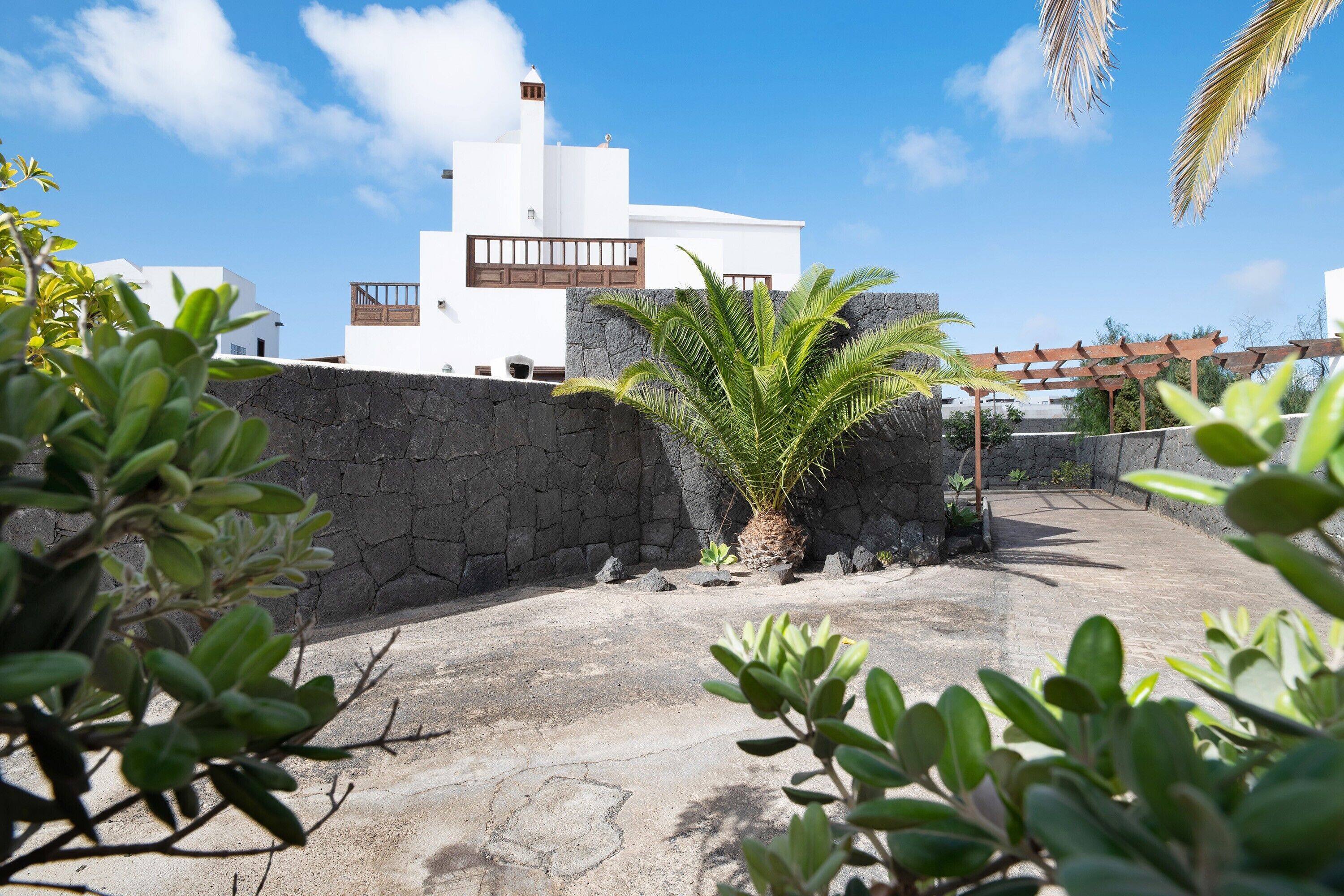 A courtyard with a stone wall, a palm tree, and a white building with a balcony.