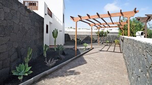 A courtyard with a stone wall, a wooden pergola, and a white building with a window. - Villa Serendipity with Mountain View, Private Heated Pool & Wi-Fi (Playa Blanca)