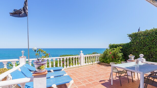A terrace with a table and chairs, a flag, and a view of the sea.