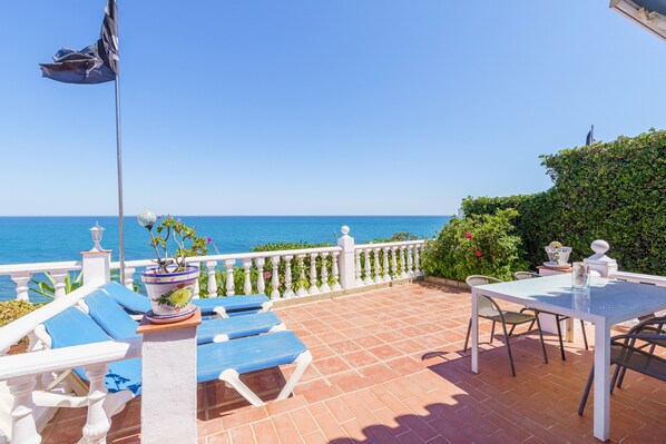 A terrace with a table and chairs, a flag, and a view of the sea.