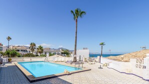 A swimming pool with a view of the sea, palm trees, and a tiled deck.