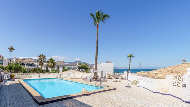 Una piscina con vista al mar, palmeras y una terraza con baldosas.