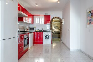 Une cuisine compacte avec des meubles rouges, un four à micro-ondes, un lave-linge et un petit four.