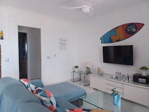 A modern living room with a sofa, glass coffee table, and a mounted surfboard.