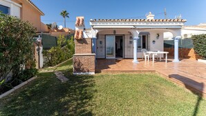 Una casa con un patio, una chimenea de ladrillo y una puerta que da a un espacio cubierto con una mesa y sillas.