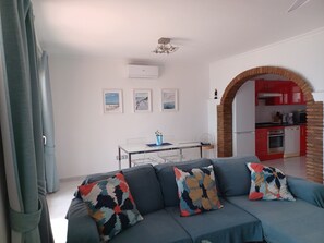 Una sala de estar con un sofá, una mesa de comedor y una cocina visible a través de un arco.