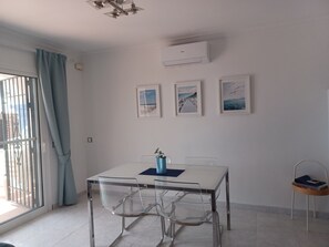 Una habitación moderna con una mesa blanca, sillas transparentes, un florero azul y cuadros en la pared.