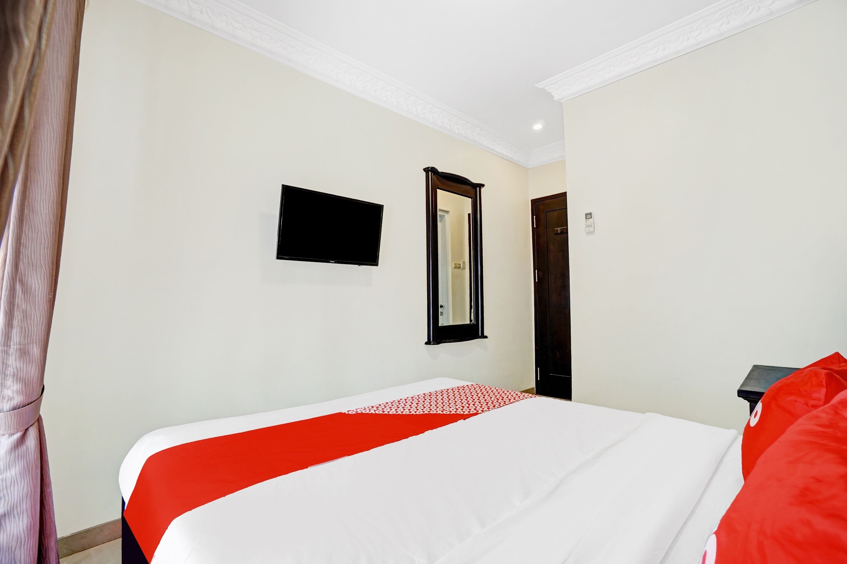 Una habitación de hotel con una cama, un televisor de pantalla plana, un espejo y una puerta.