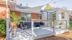 En täckt uteplats med utemöbler, en krukväxt och ett hus i tegel som syns i bakgrunden.