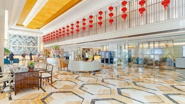 A spacious lobby with a high ceiling, a reception desk, and a patterned floor.