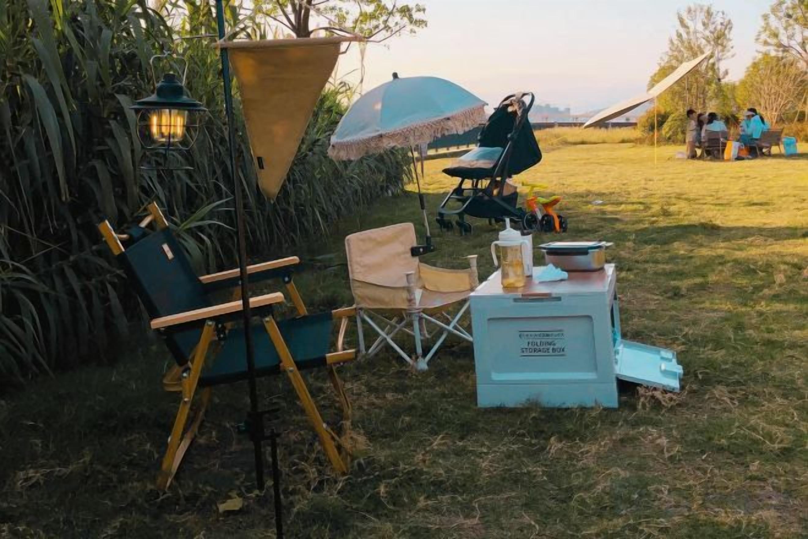 An outdoor camping setup with a tent, folding chairs, a lantern, and a cooler.
