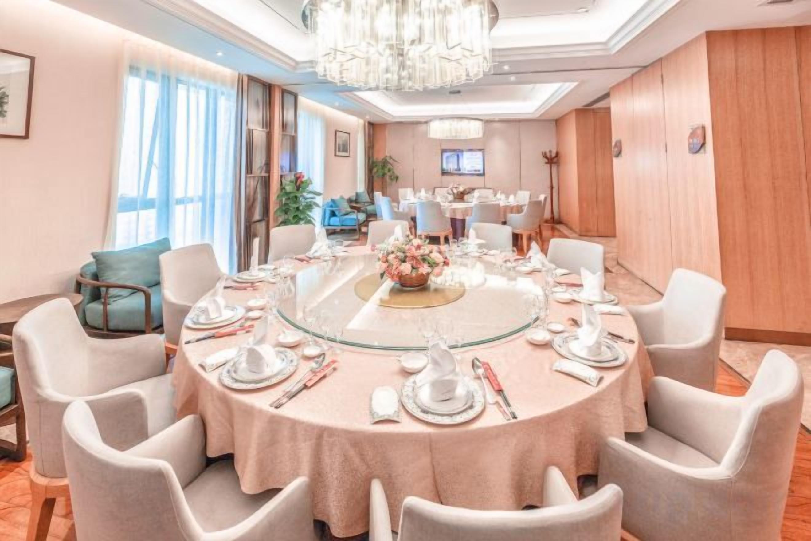 A round dining table with chairs, set for a meal, in a well-lit room with a chandelier.