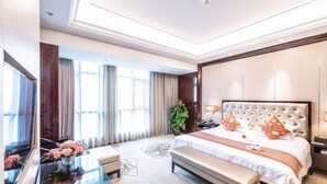 A modern hotel room with a large bed, a bench, a desk, and a TV.