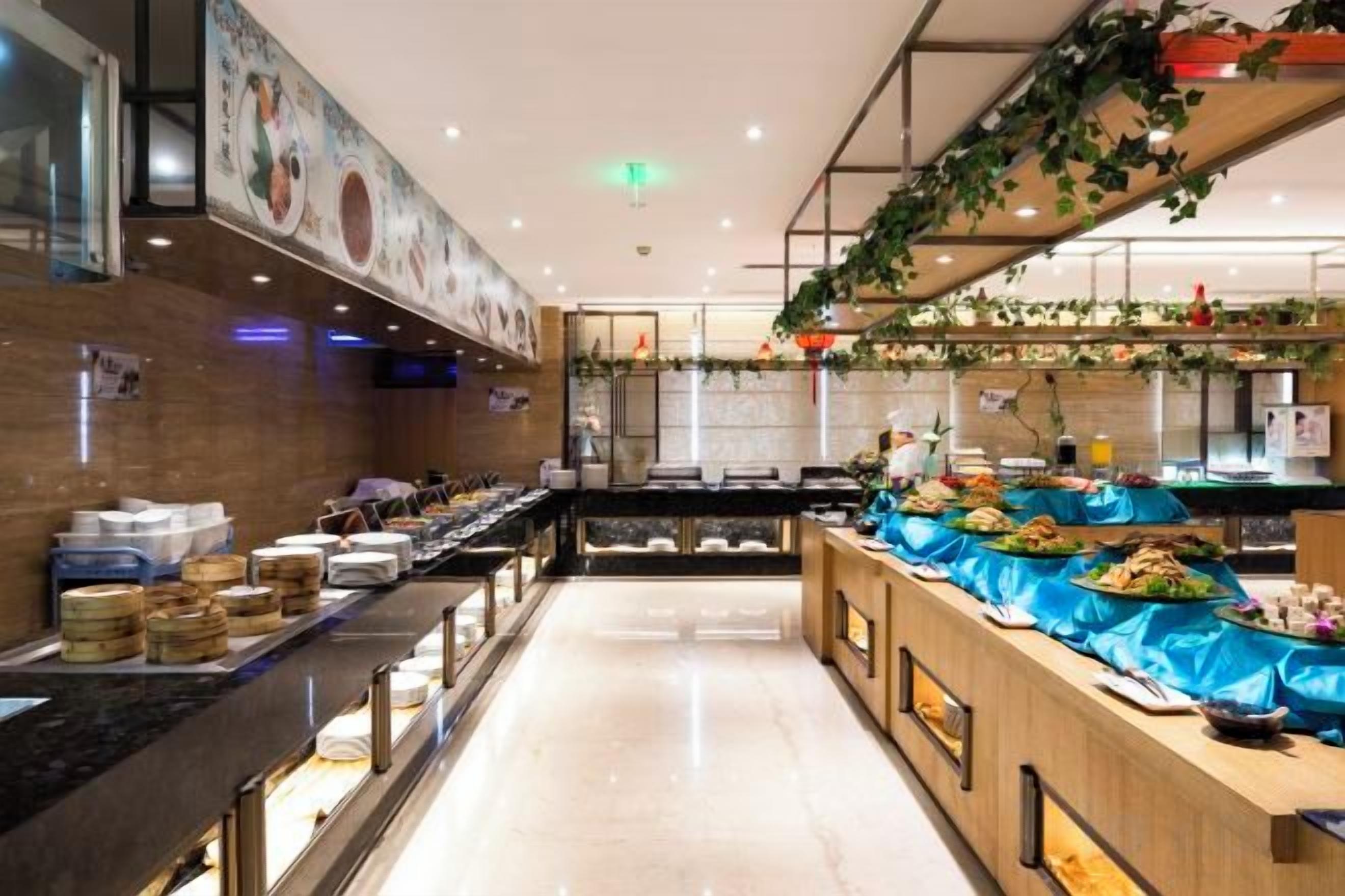 A buffet area with a variety of food items displayed on tables, a counter with food containers, and a tiled wall with a mural.
