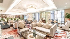 A spacious lobby with multiple seating areas, including sofas and armchairs, arranged around a central coffee table.