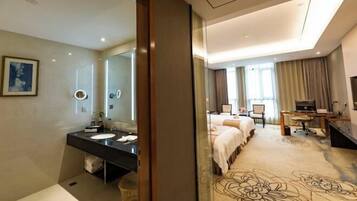 A hotel room with a large bed, a desk, a chair, a TV, and a bathroom with a sink and mirror.