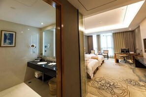 Hotelkamer met een groot bed, een bureau, een stoel, een televisie en een badkamer met wastafel en spiegel.