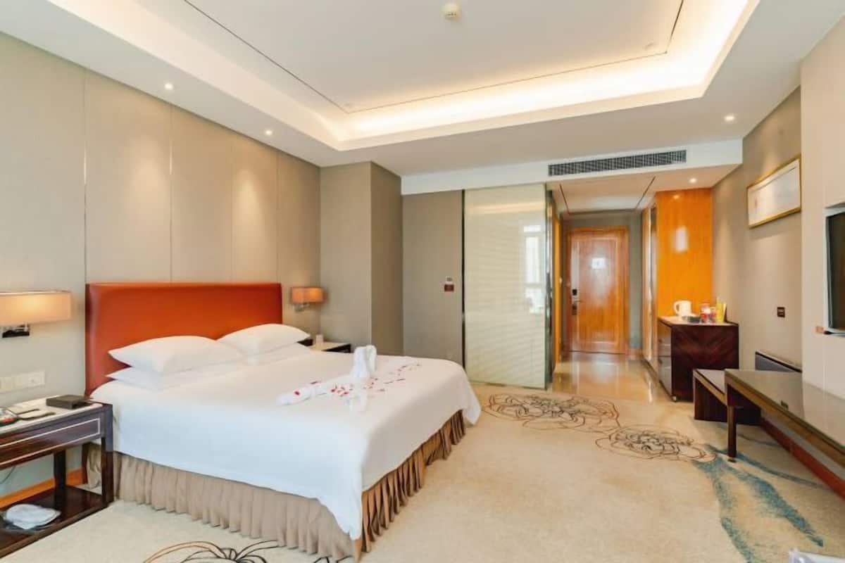 A hotel room with a large bed, bedside tables, a desk, a chair, a TV, and a bathroom with a shower and toilet.