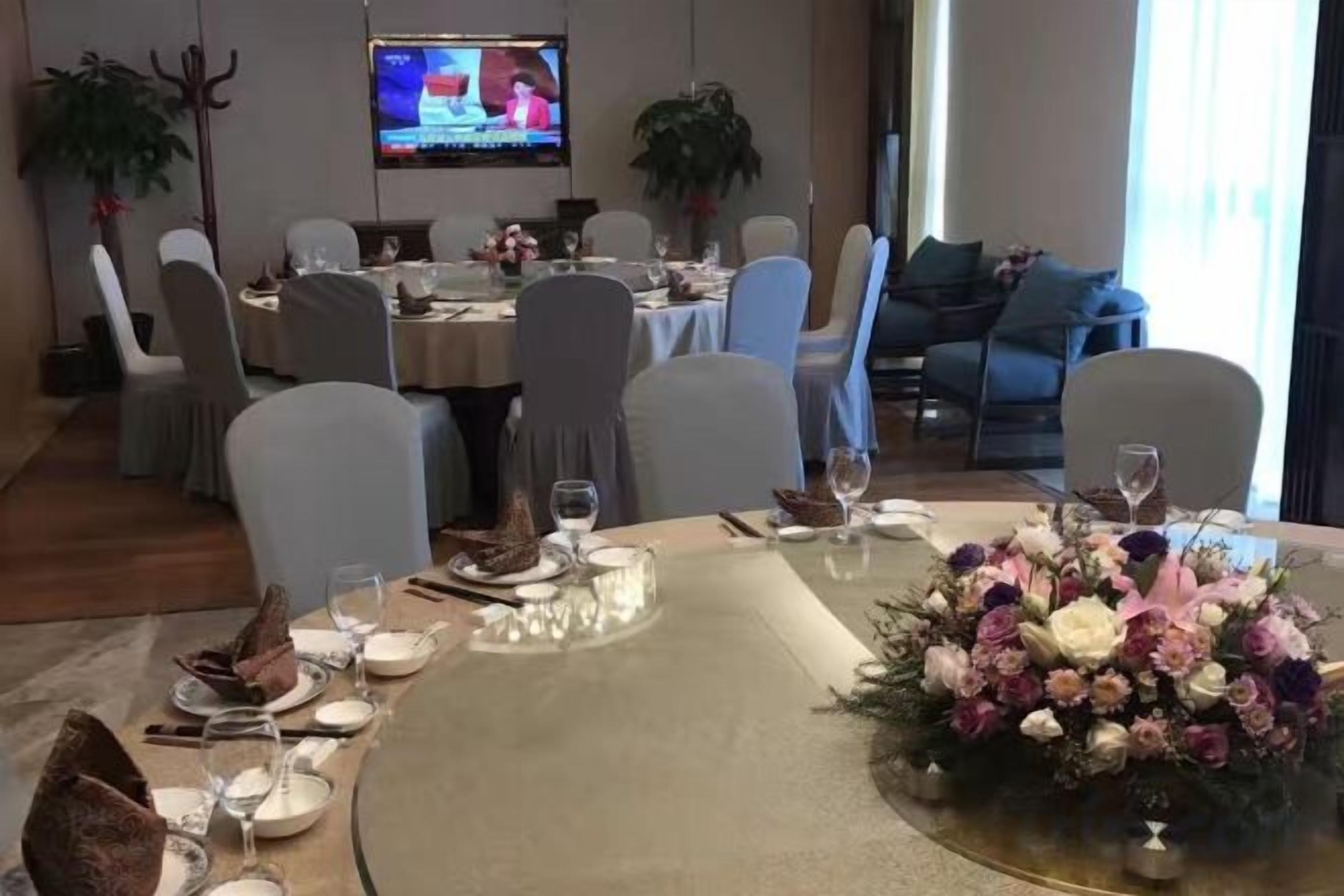 A dining area with round tables, chairs, and a television screen in the background.
