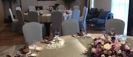 A dining area with round tables, chairs, and a television screen in the background.