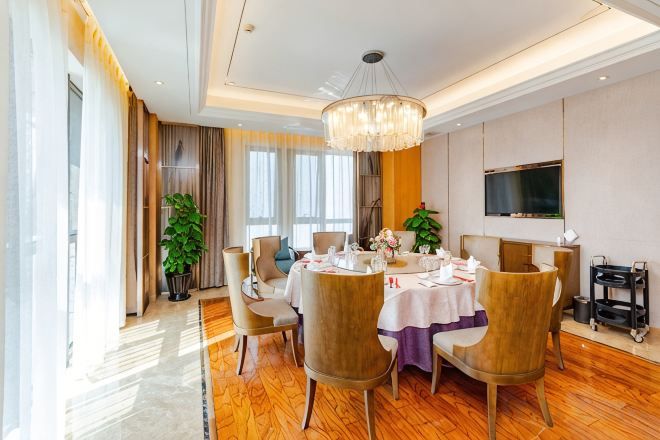 A dining area with a round table, chairs, a chandelier, and a television on the wall.