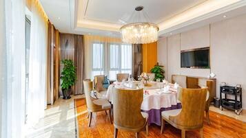 A dining area with a round table, chairs, a chandelier, and a television on the wall.