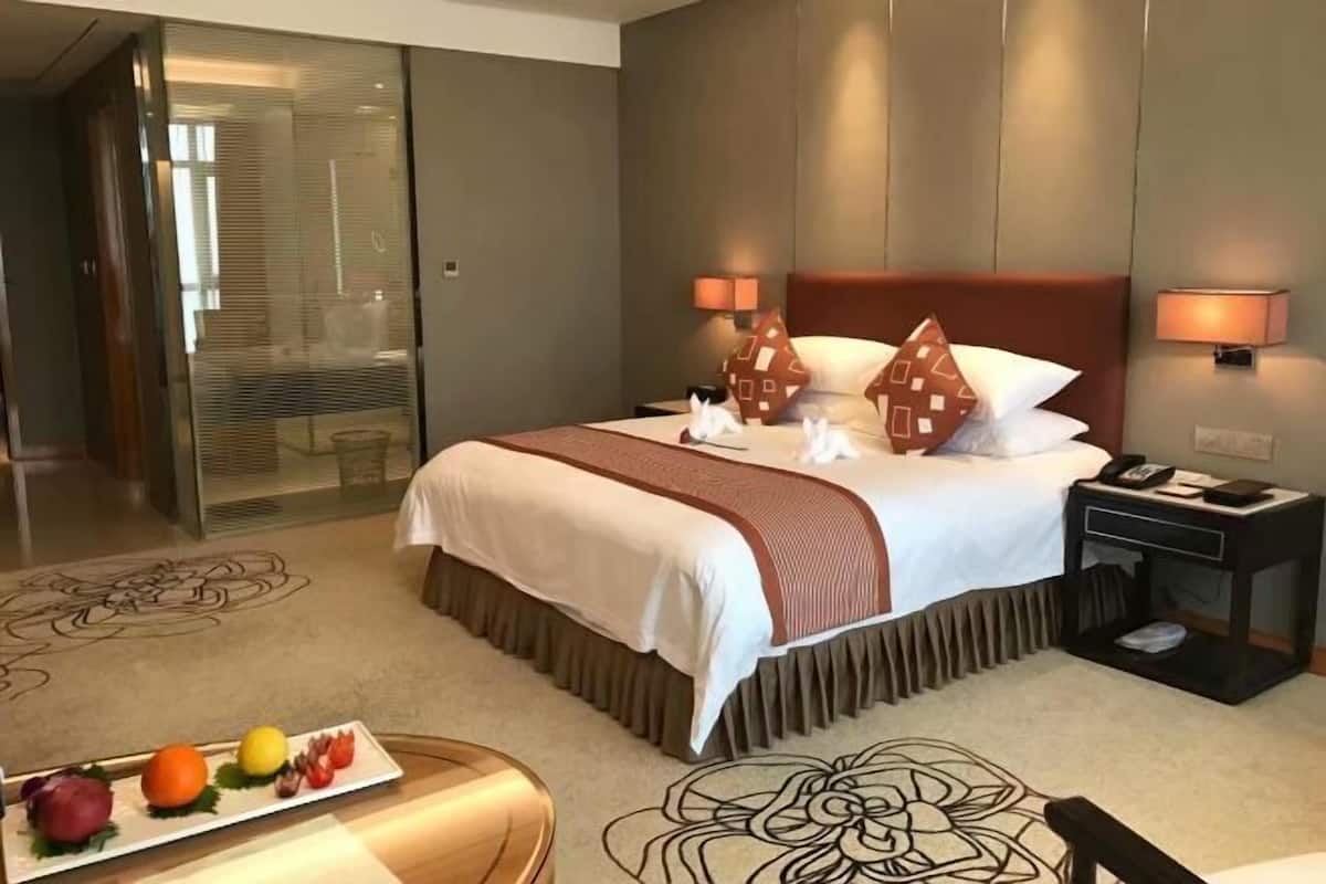 A hotel room with a bed, bedside lamps, a nightstand, a fruit plate, and a patterned carpet.
