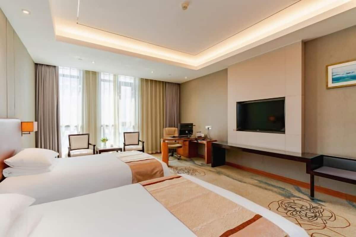 A hotel room with two beds, a desk, a TV, and a view of the outdoors.