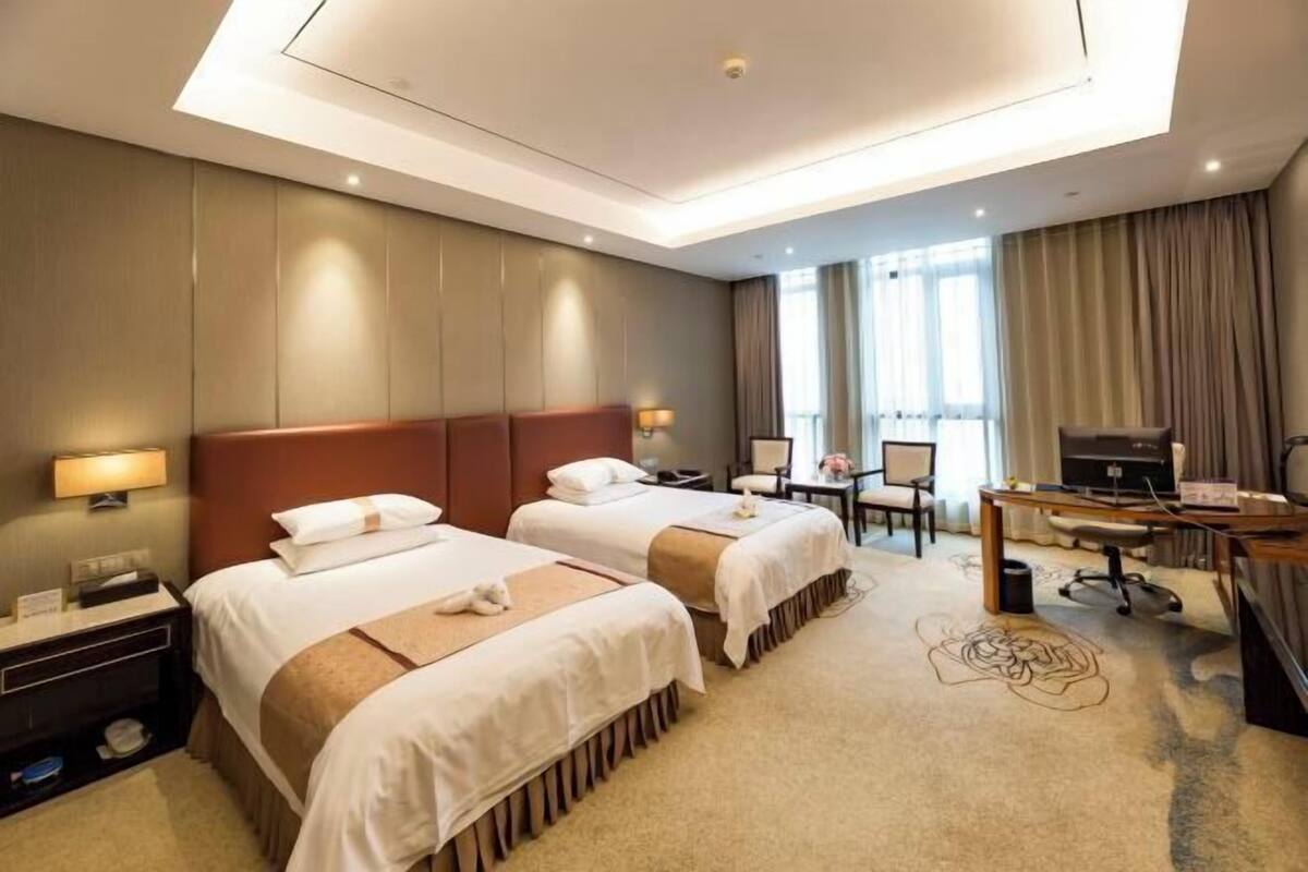 A hotel room with two beds, a desk, a TV, and a window with curtains.