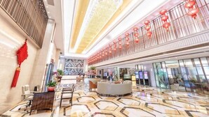 A spacious lobby with a high ceiling, a reception desk, seating areas, and a decorative railing with red lanterns.