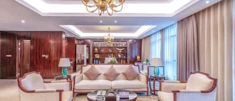 A spacious living area with a sofa, armchairs, a coffee table, a chandelier, and a bookshelf.