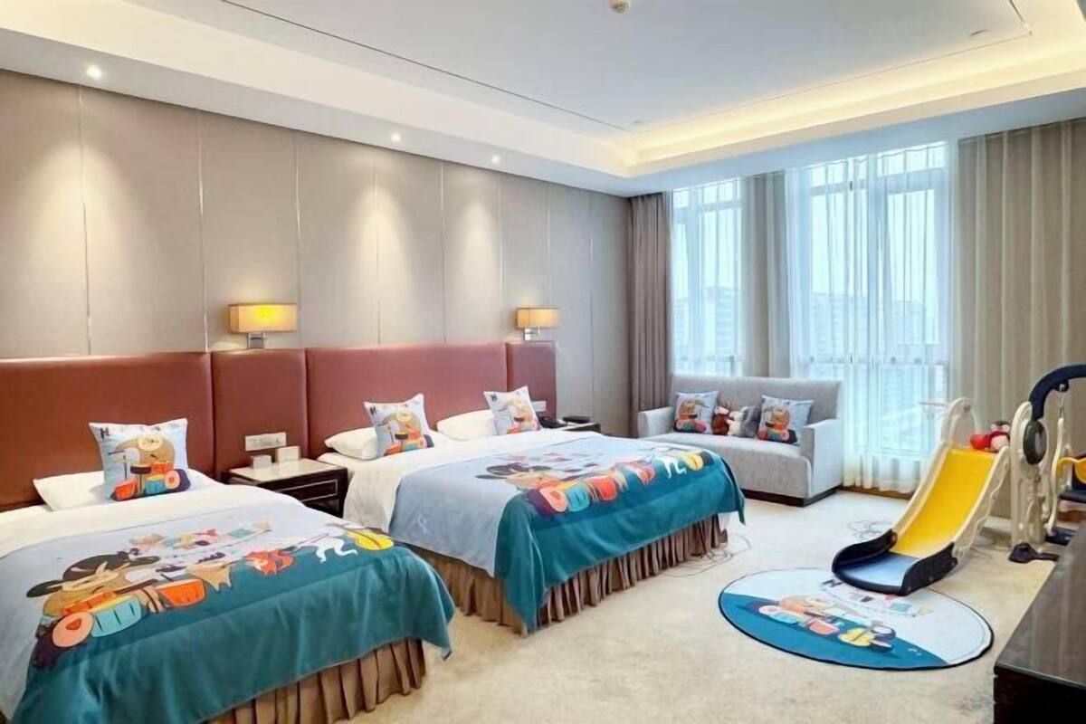A hotel room with two beds, a sofa, a children's play area, and large windows.