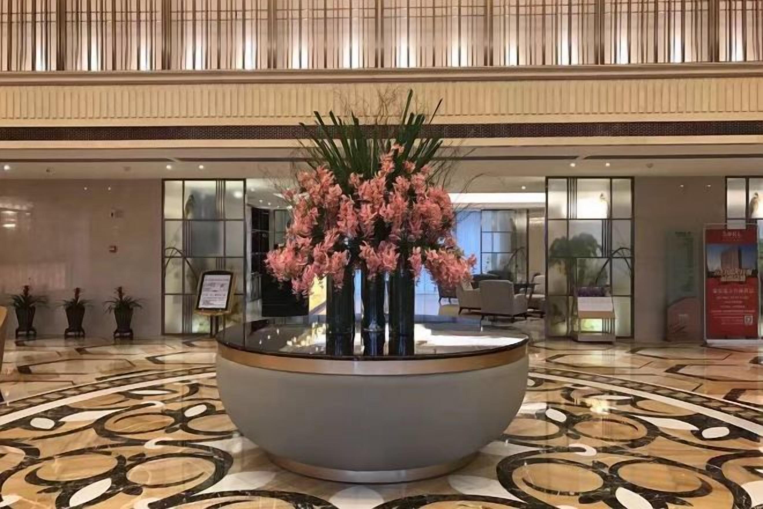 A lobby with a large floral arrangement in a bowl, a patterned floor, and a reception area with a desk and chairs.