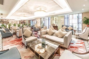 A spacious lobby with multiple seating areas, a central coffee table, and large windows providing natural light.