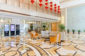 Een hotel lobby met een hoge plafond, een receptiebalie, een zithoek en een decoratieve wand.